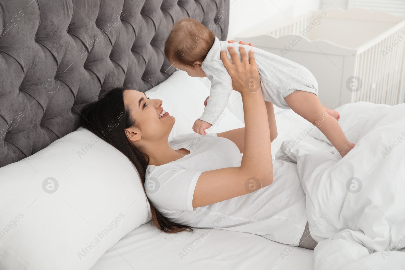 Photo of Young mother playing with her cute baby on bed indoors