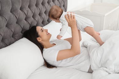 Young mother playing with her cute baby on bed indoors