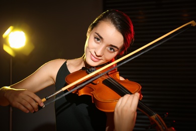 Beautiful young woman playing violin in dark room