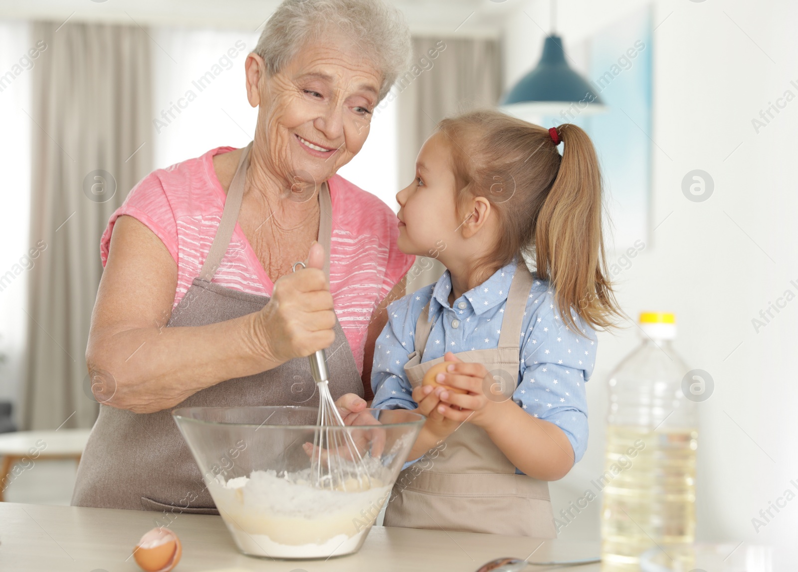 Photo of Cute girl and her grandmother cooking in kitchen