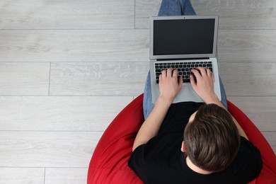 Photo of Man working with laptop in beanbag chair, top view. Space for text