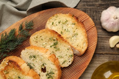 Tasty baguette with garlic, dill and oil on wooden table, flat lay