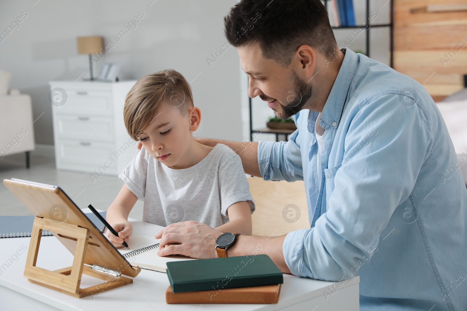 Photo of Boy with father doing homework at table indoors