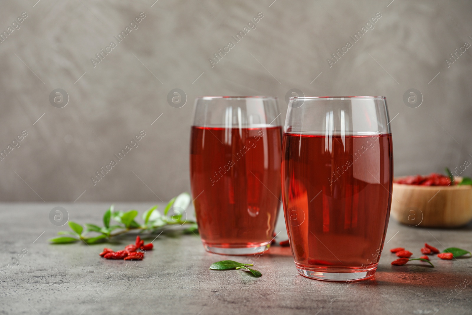 Photo of Glasses of healthy goji juice on grey table. Space for text