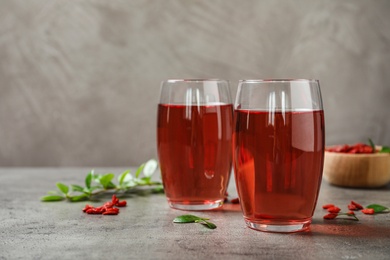 Photo of Glasses of healthy goji juice on grey table. Space for text