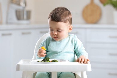 Photo of Cute little baby eating healthy food in high chair at home