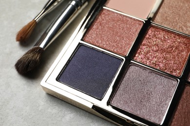 Photo of Beautiful eye shadow palette and brushes on grey table, closeup