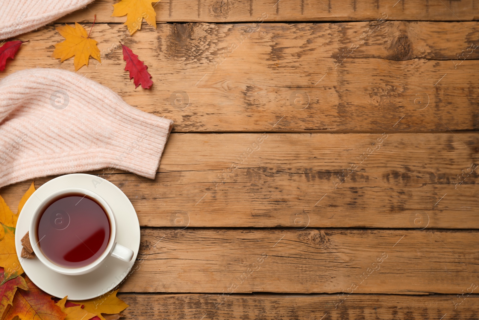 Photo of Cup of hot tea, sweater and autumn leaves on wooden table, flat lay. Space for text