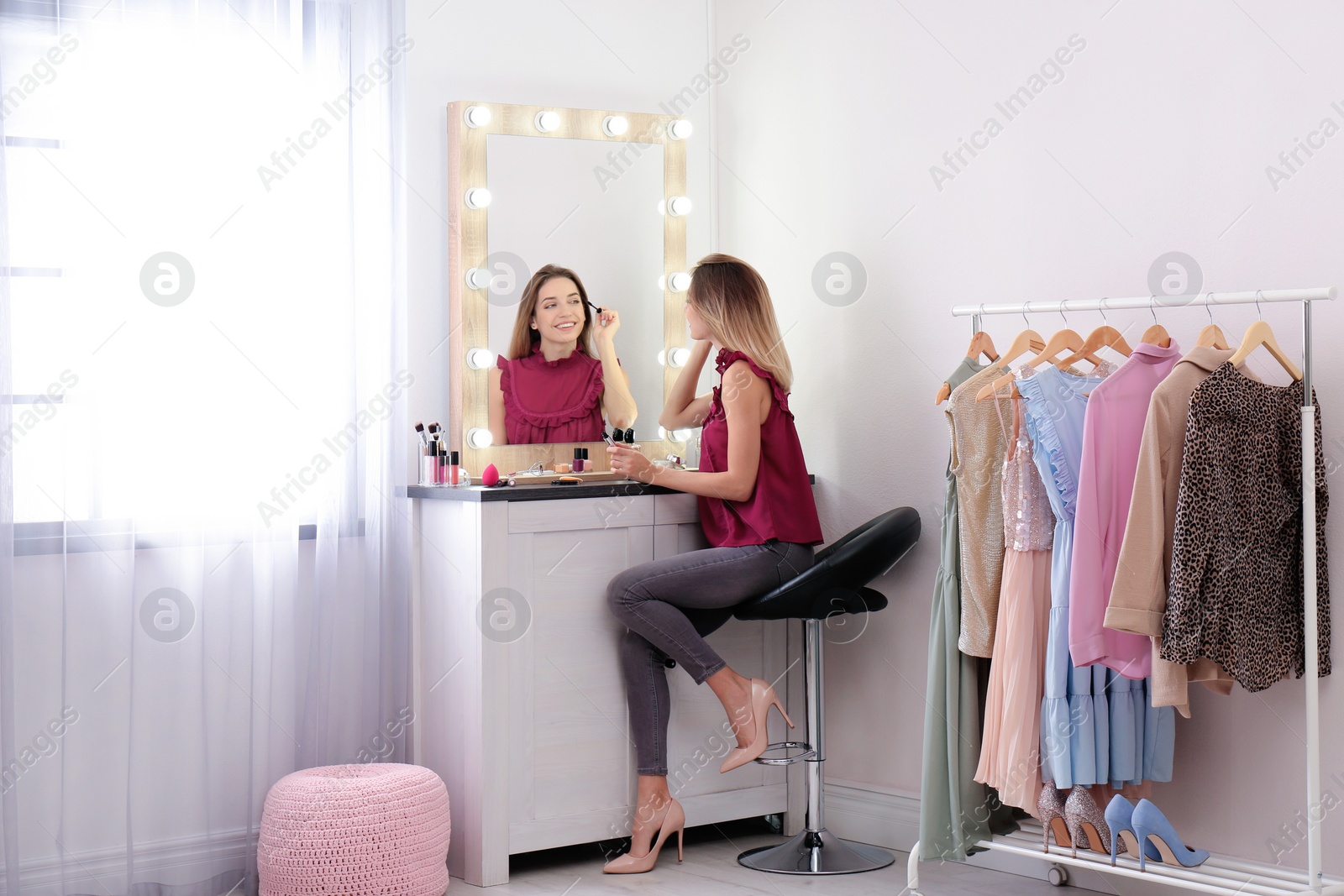 Photo of Woman applying makeup near mirror with light bulbs in dressing room