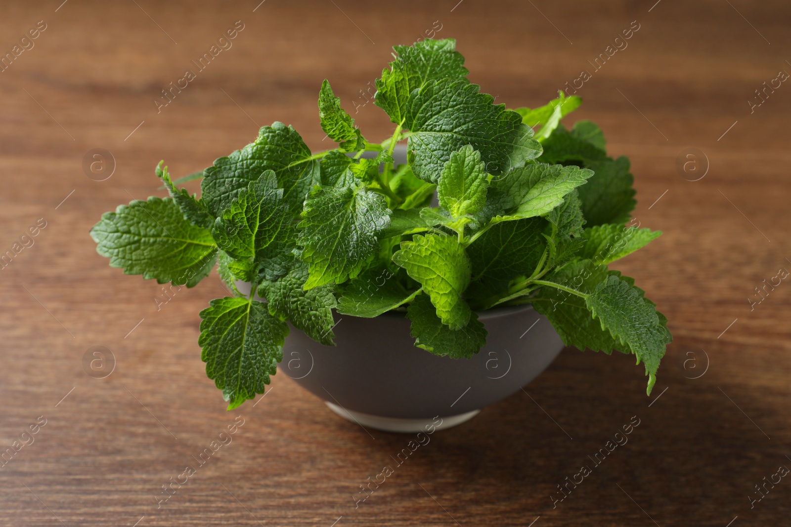 Photo of Fresh lemon balm in bowl on wooden table