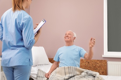 Photo of Nurse talking with senior man in hospital ward. Medical assisting