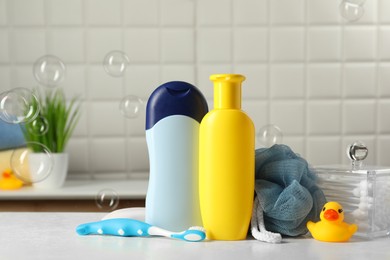 Photo of Baby cosmetic products, bath duck, toothbrush and sponge on white table against soap bubbles