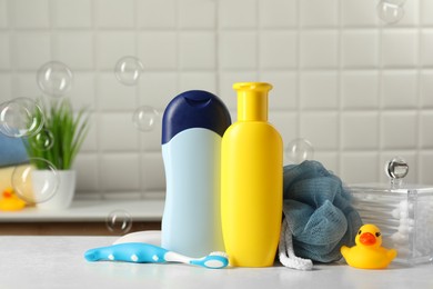 Baby cosmetic products, bath duck, toothbrush and sponge on white table against soap bubbles