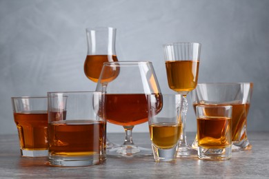 Photo of Different liqueurs in glasses on grey textured table