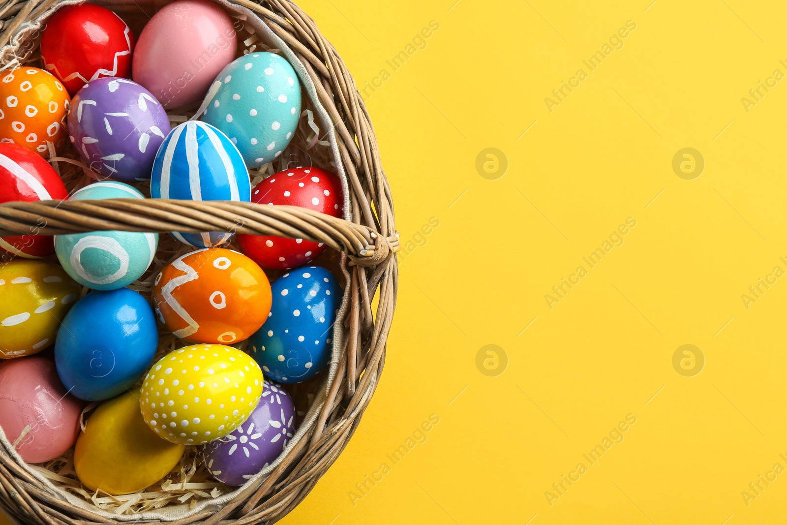 Photo of Wicker basket with painted Easter eggs on color background, top view. Space for text