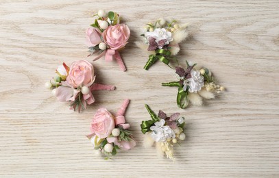 Photo of Stylish boutonnieres on white wooden table, flat lay