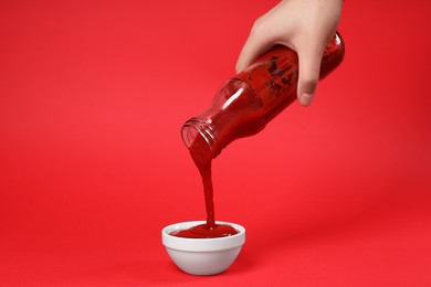 Photo of Woman pouring tasty ketchup from bottle into bowl on red background, closeup