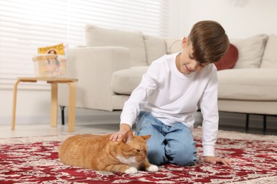 Little boy petting cute ginger cat on carpet at home