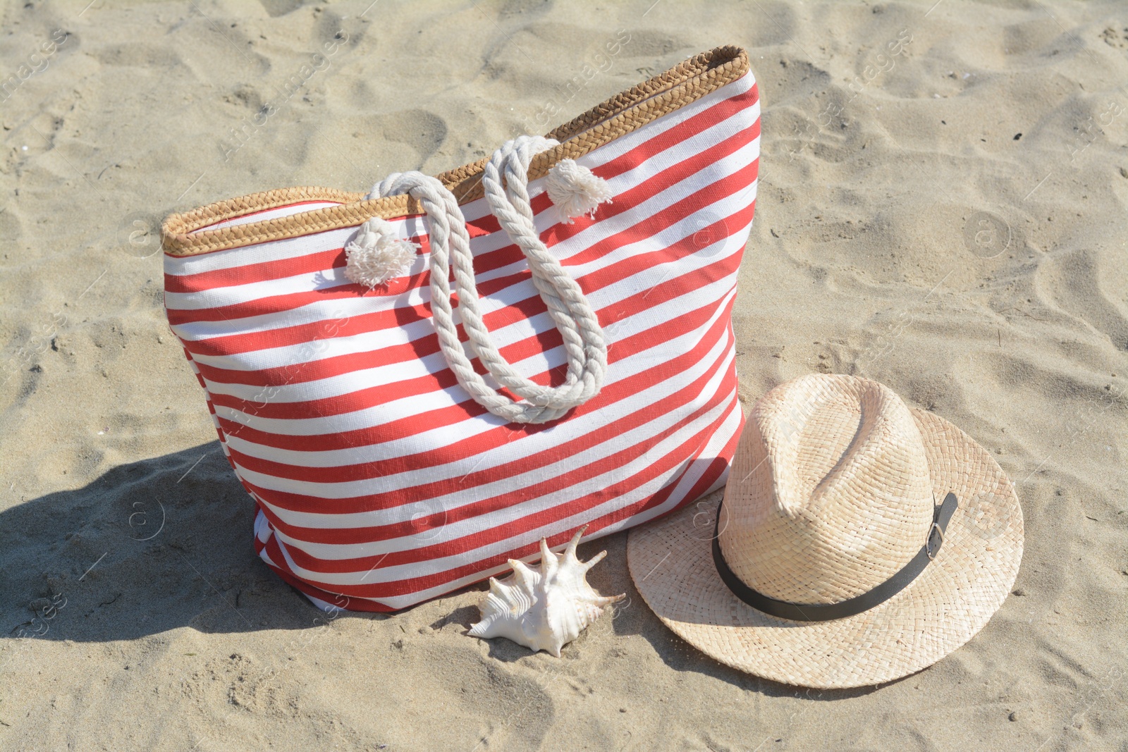 Photo of Stylish striped bag with straw hat and seashell on sandy beach