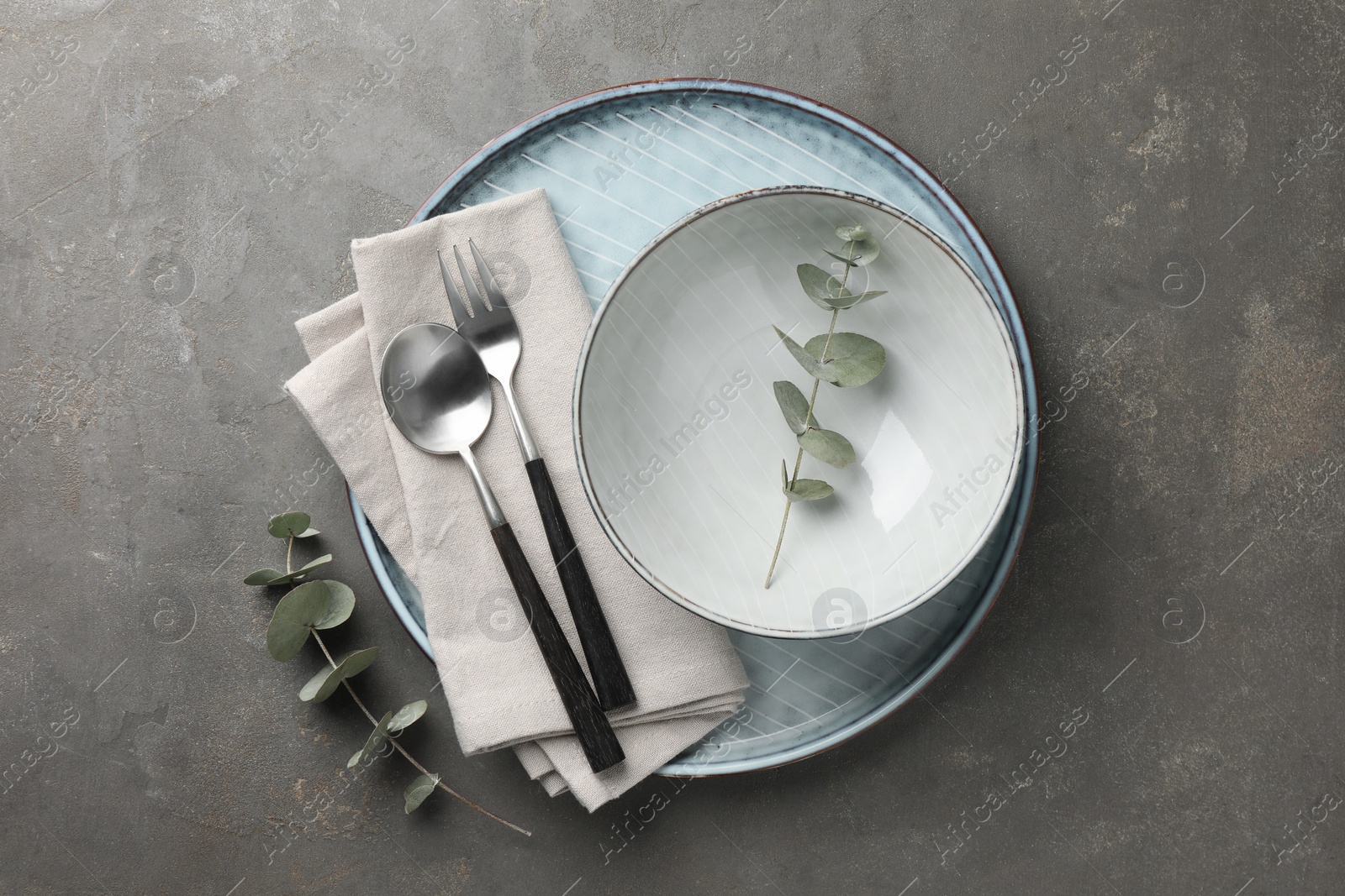 Photo of Stylish setting with cutlery, napkin, eucalyptus branches and plate on grey table, top view