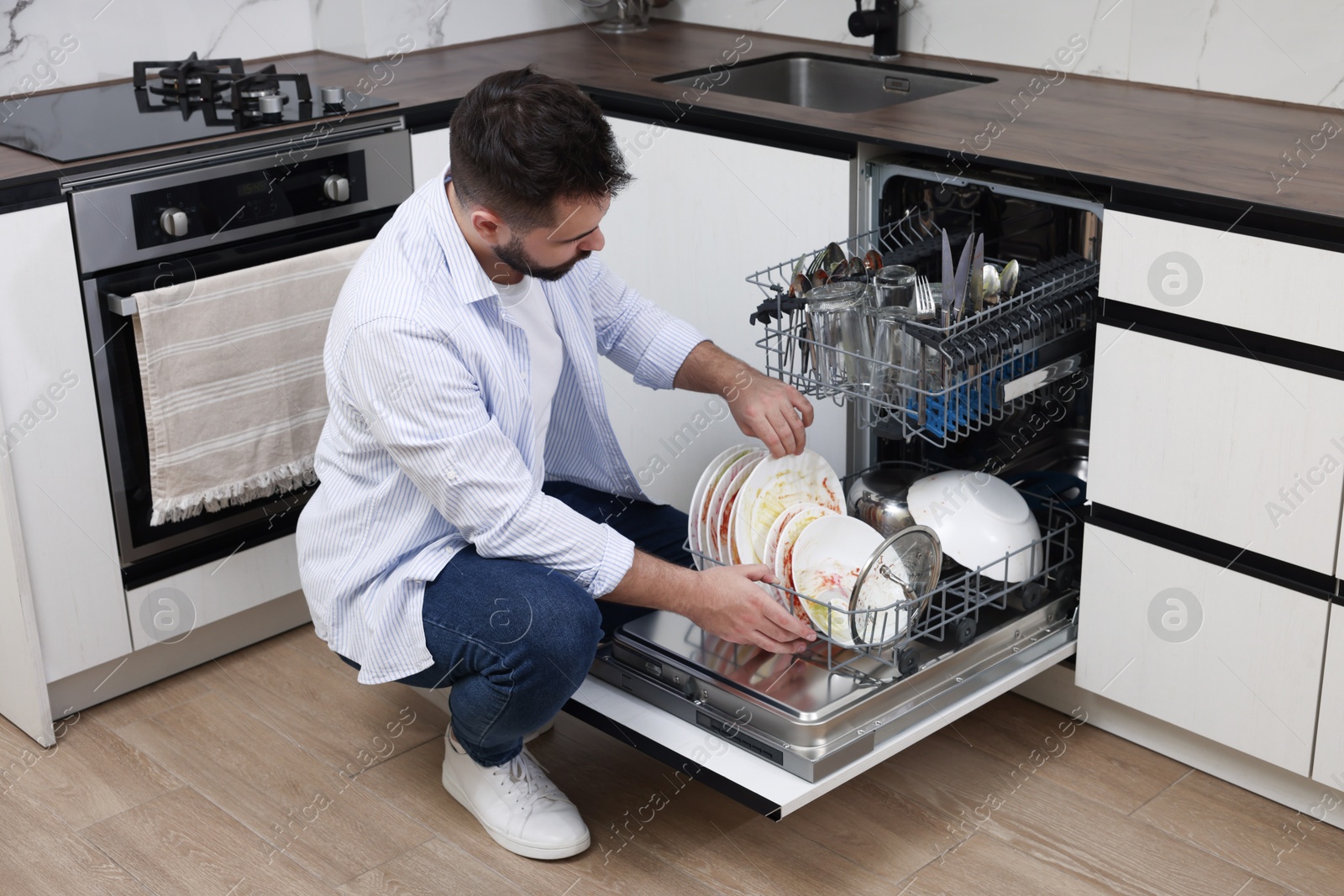 Photo of Man loading dishwasher with dirty plates indoors