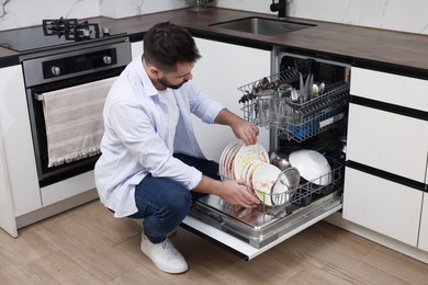 Photo of Man loading dishwasher with dirty plates indoors