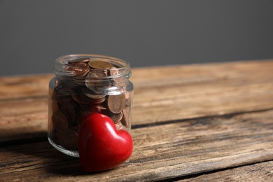 Red heart and donation jar with coins on wooden table against grey background. Space for text