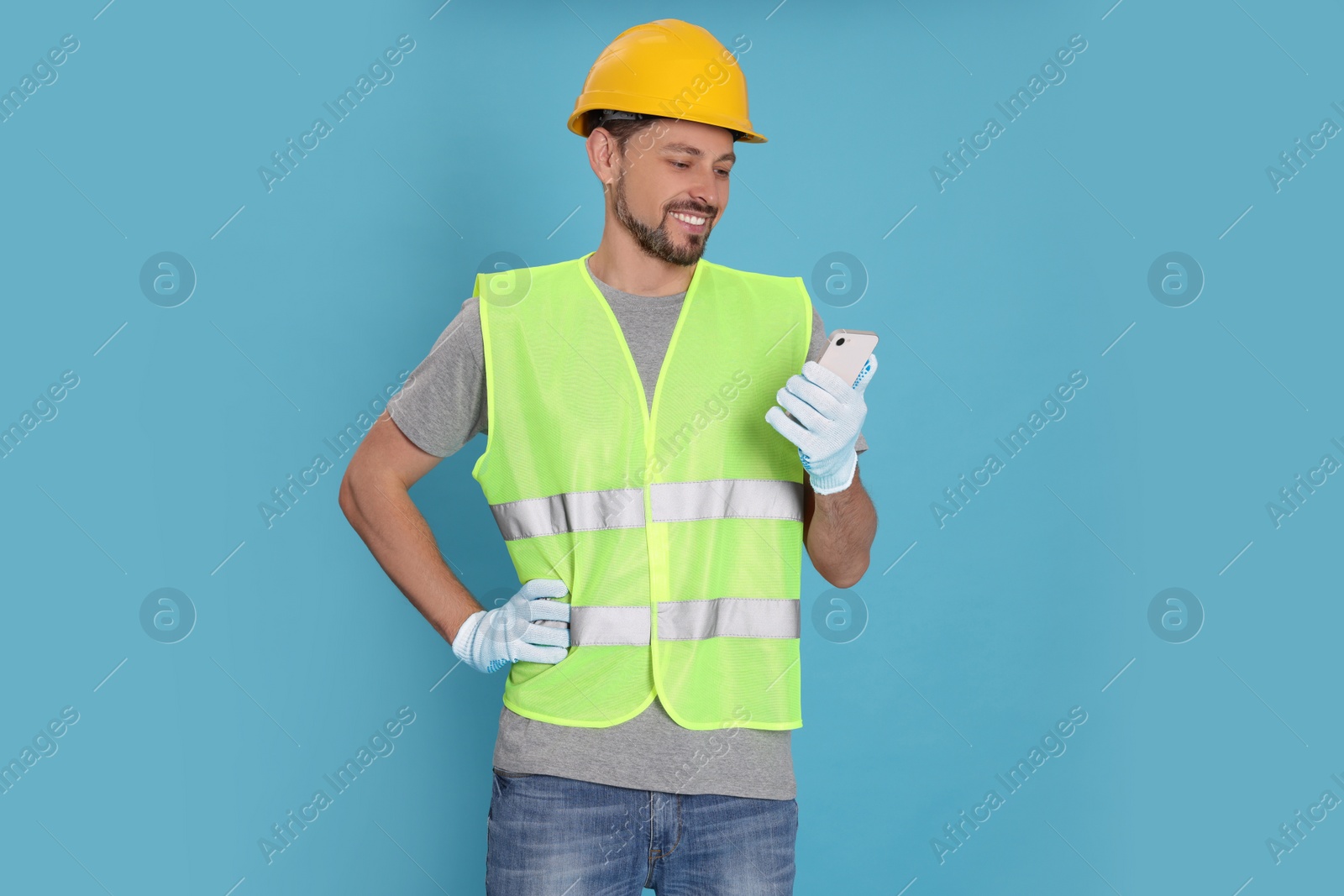 Photo of Male industrial engineer in uniform with phone on light blue background