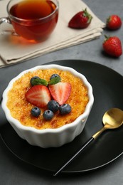 Delicious creme brulee with berries and mint in bowl on grey table, closeup