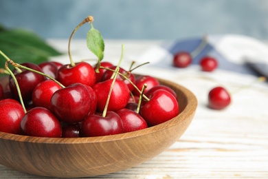 Bowl with ripe sweet cherries on white wooden table, closeup. Space for text