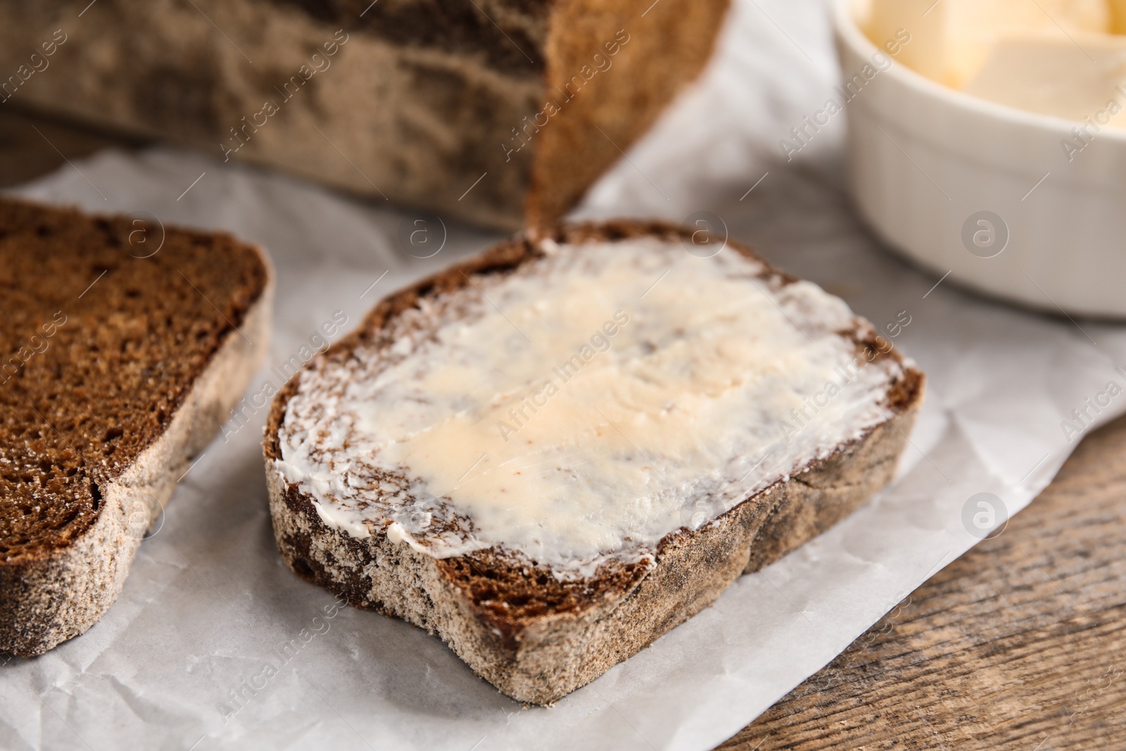 Photo of Slice of rye bread with butter on wooden table, closeup