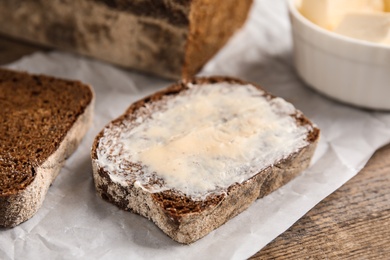 Slice of rye bread with butter on wooden table, closeup