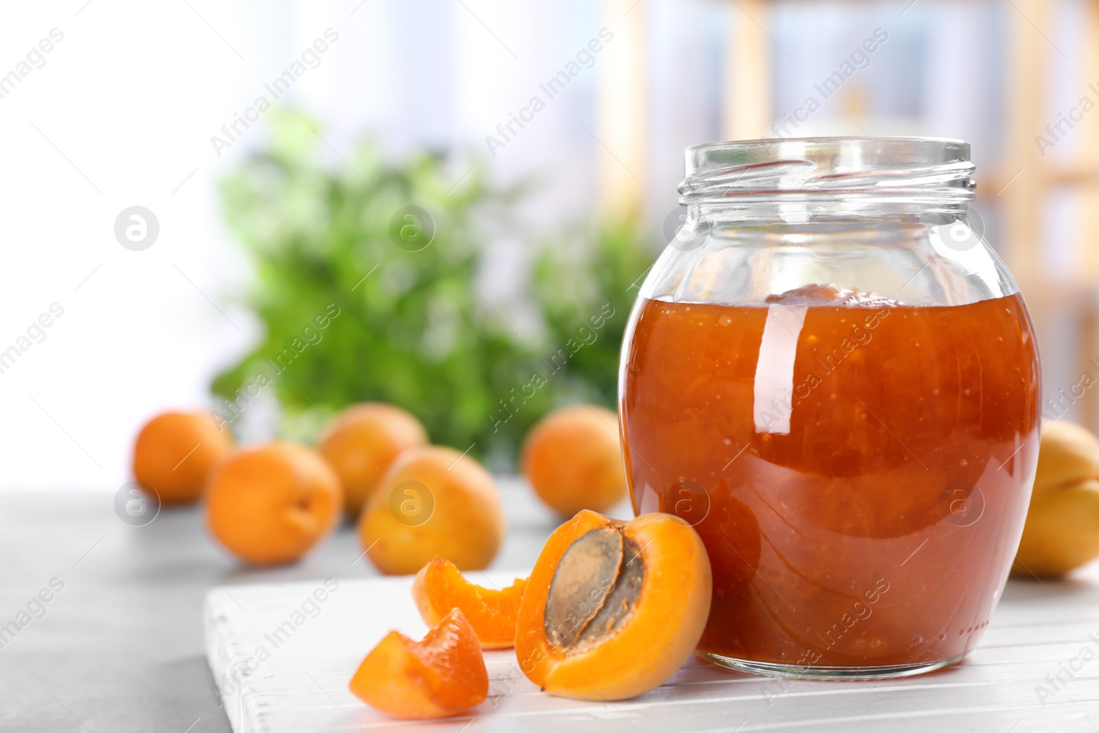 Photo of Jar with tasty apricot jam on wooden board