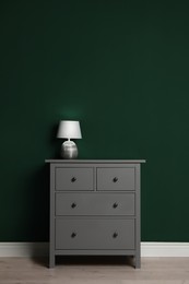 Modern chest of drawers with lamp near green wall indoors