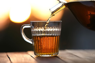 Pouring delicious tea into glass cup on wooden table against blurred background, closeup