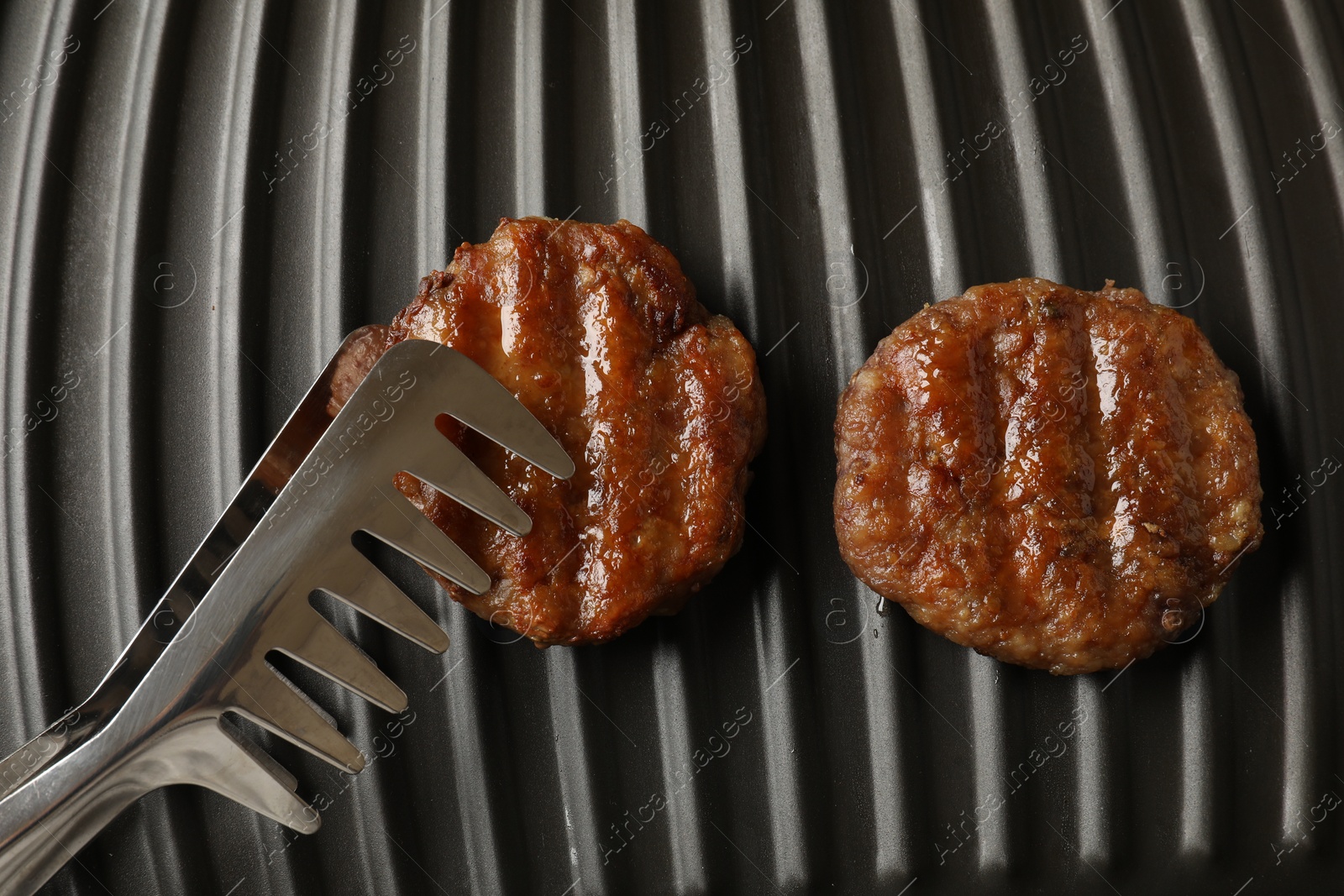 Photo of Taking delicious hamburger patty with tongs from electric grill, top view