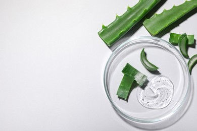 Petri dish with cosmetic gel and cut aloe vera on white background, flat lay. Space for text