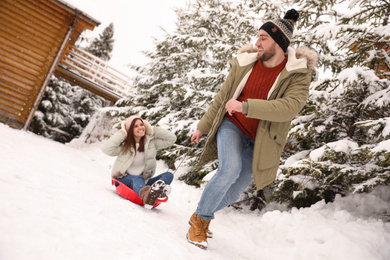 Young man pulling sled with his girlfriend outdoors on snowy day. Winter vacation