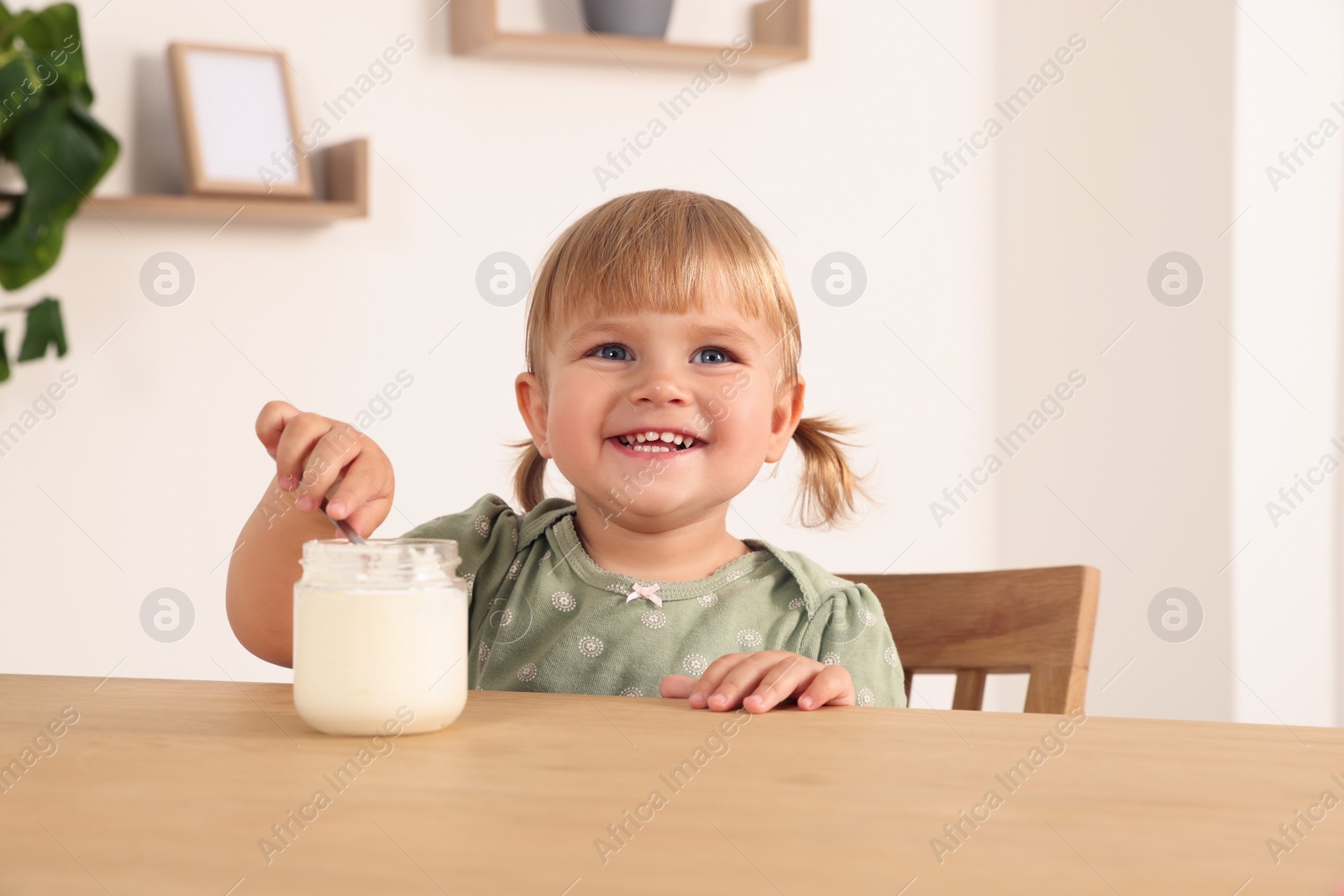 Photo of Cute little child eating tasty yogurt with spoon at wooden table indoors