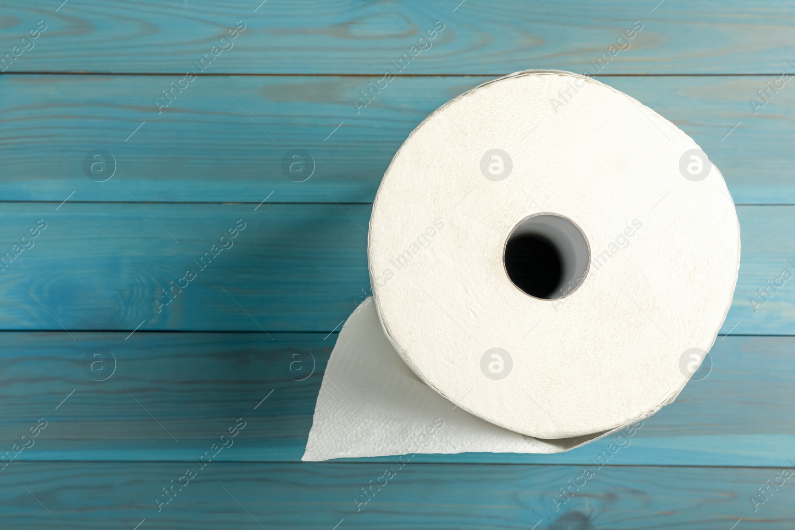 Photo of Roll of white paper towels on light blue wooden table, top view. Space for text