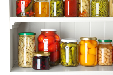 Photo of Jars of pickled fruits and vegetables on white wooden shelves