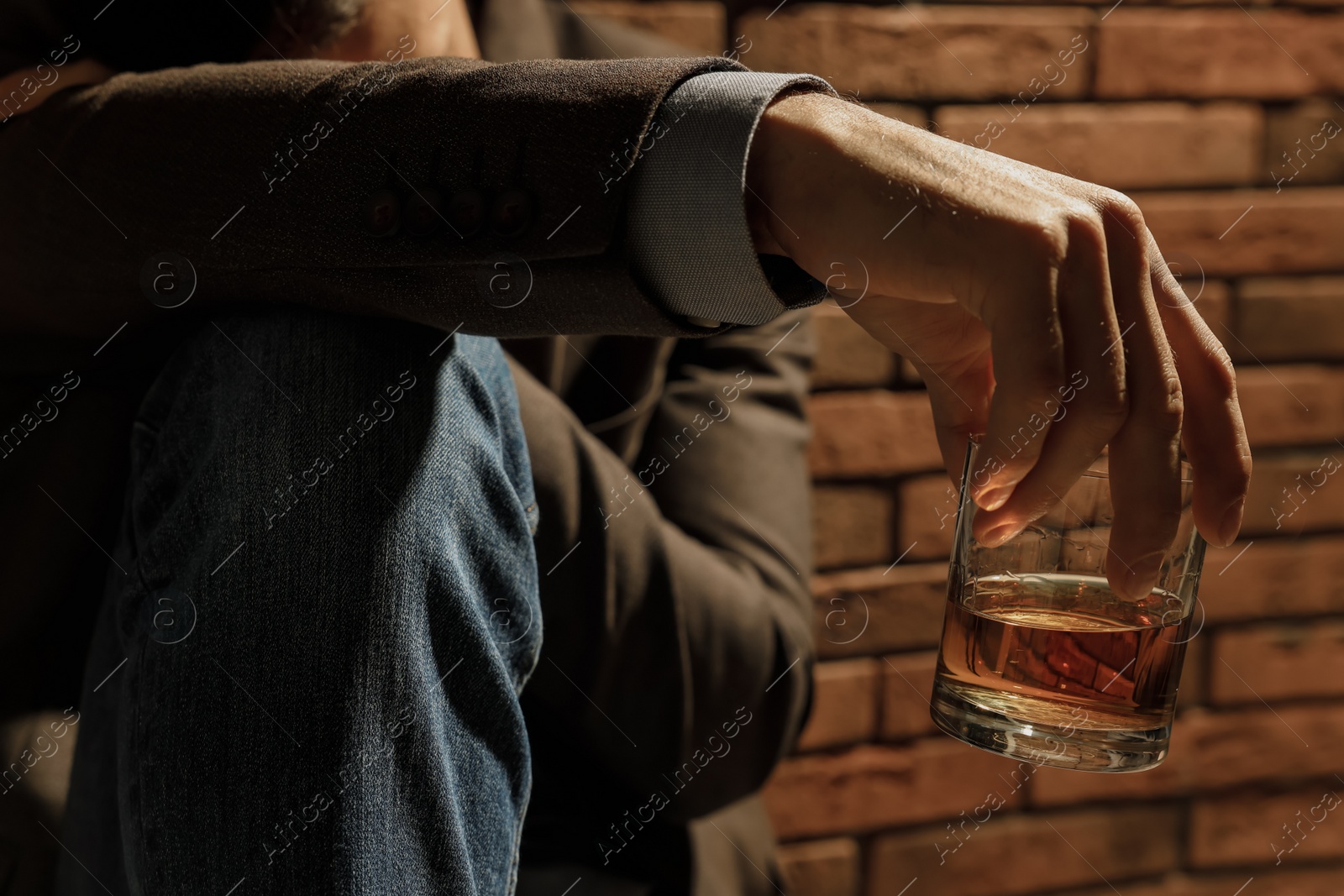 Photo of Addicted man with glass of alcoholic drink near red brick wall, closeup