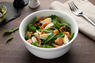 Delicious salad with boiled eggs, salmon and arugula on wooden table, closeup