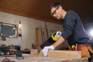 Photo of Professional carpenter sawing wooden plank at workbench