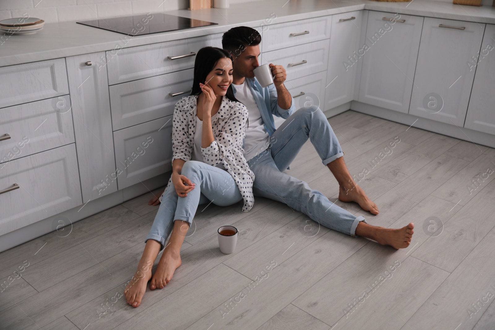 Photo of Happy couple sitting on warm floor in kitchen. Heating system