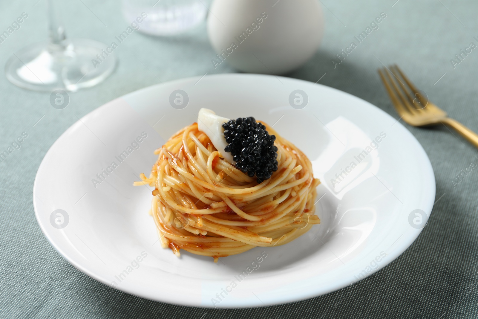 Photo of Tasty spaghetti with tomato sauce and black caviar served on table, closeup. Exquisite presentation of pasta dish