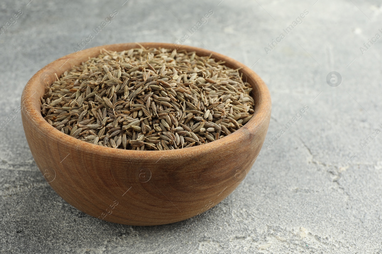 Photo of Bowl of caraway seeds on grey table, closeup