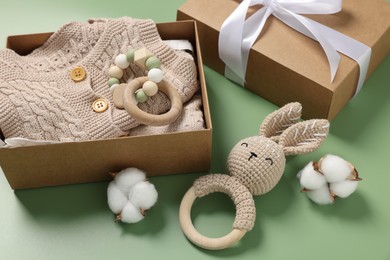 Different baby accessories, knitted clothes and cotton flowers on green background