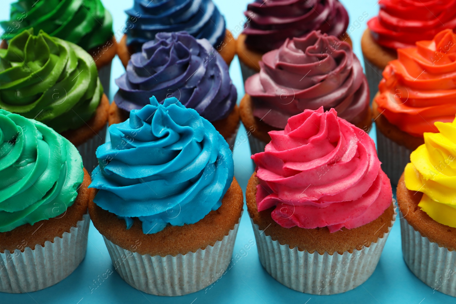 Photo of Many delicious colorful cupcakes on light blue background, closeup