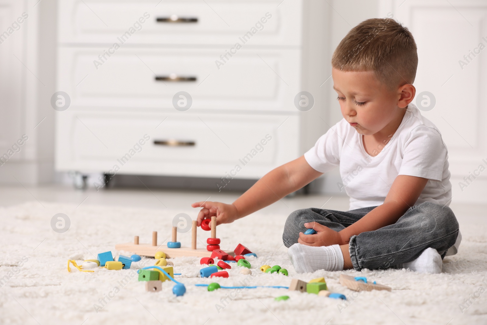 Photo of Motor skills development. Little boy playing with stacking and counting game on floor indoors